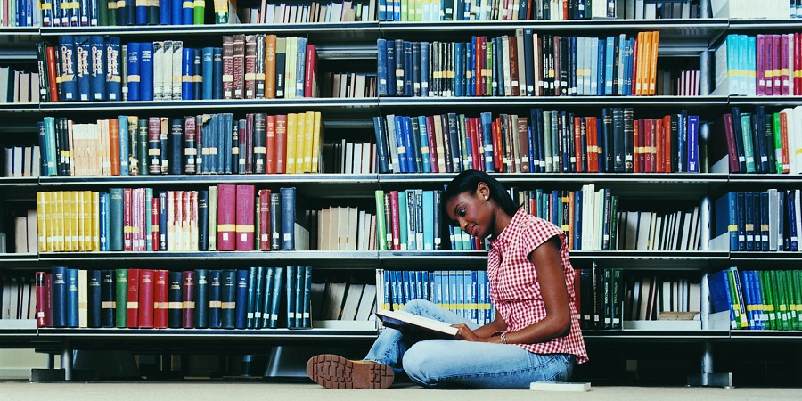 Female University Student Sitting on a Library Floor Reading a Book